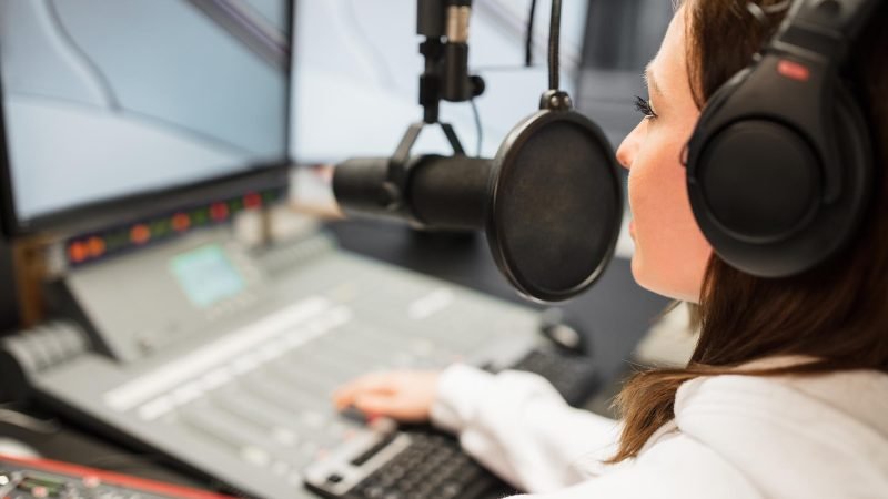 Jockey Wearing Headphones While Using Microphone In Radio Statio Young female jockey wearing headphones while using microphone in radio station